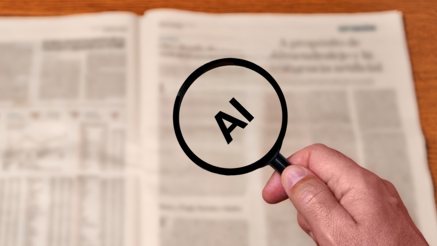 A magnifying glass highlighting the letters "AI" over a blurred newspaper background.