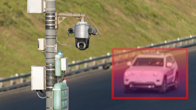 A security camera mounted on a pole, with a red digital box around a car.