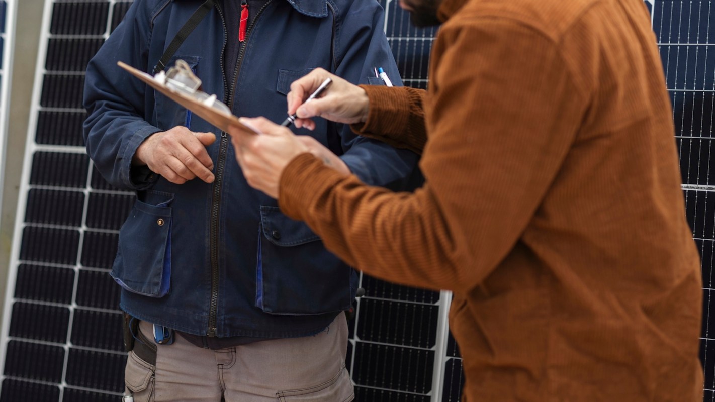 Two people discussing near solar panels, one holding a clipboard and the other gesturing.