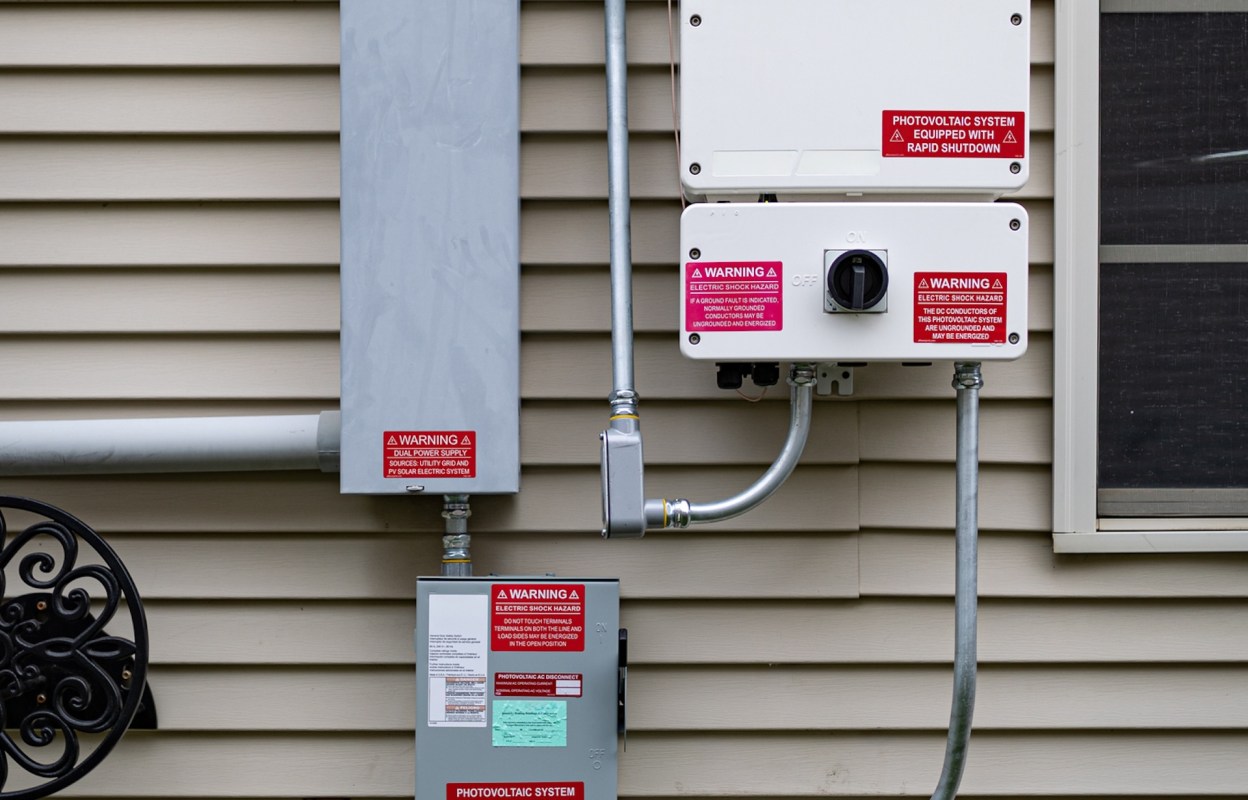 Photovoltaic electrical equipment with warning labels mounted on a house wall.