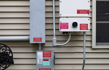 Photovoltaic electrical equipment with warning labels mounted on a house wall.