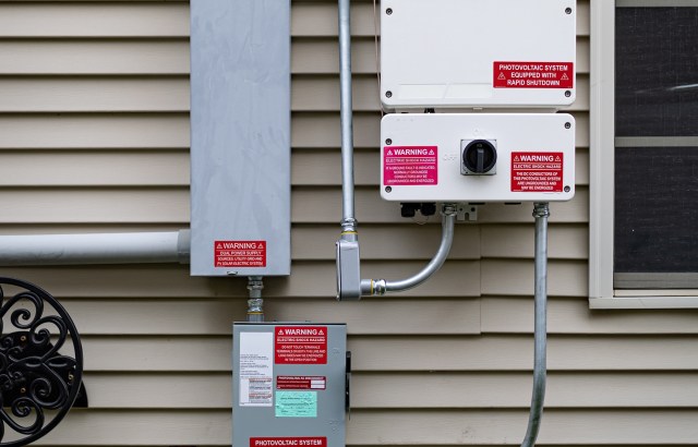Photovoltaic electrical equipment with warning labels mounted on a house wall.