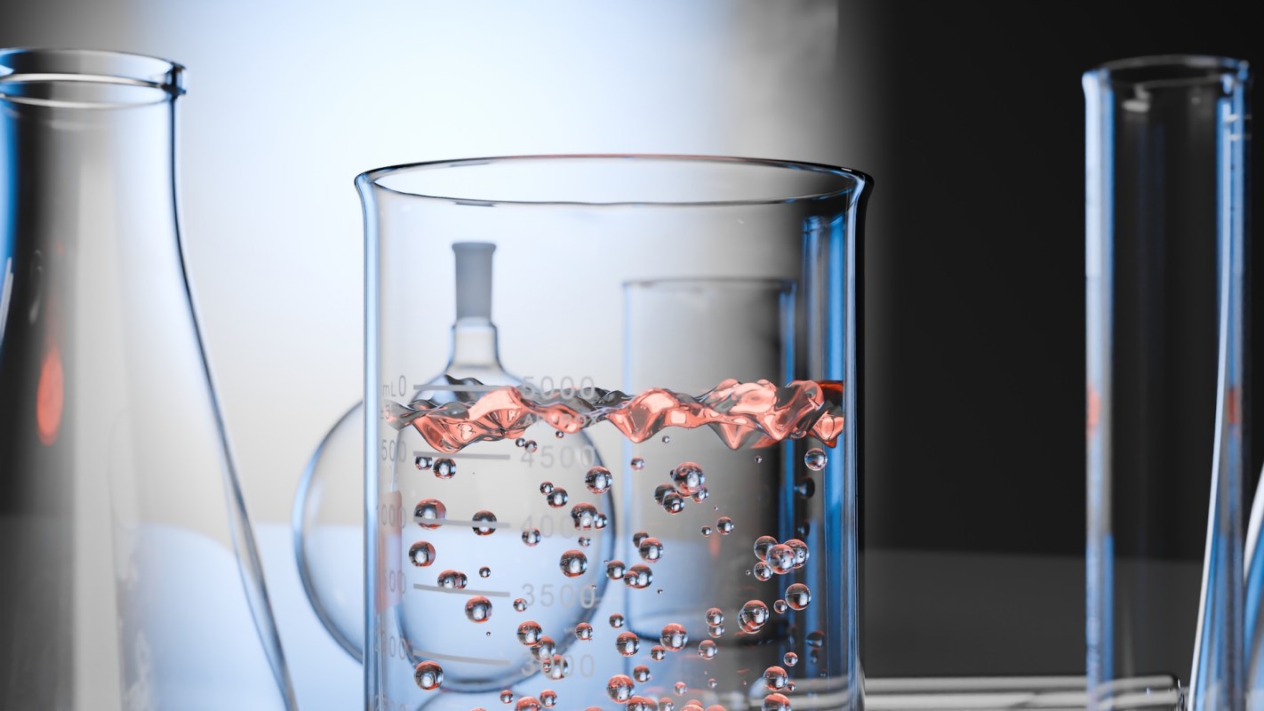 A glass beaker filled with a pink liquid and bubbles, surrounded by laboratory glassware.