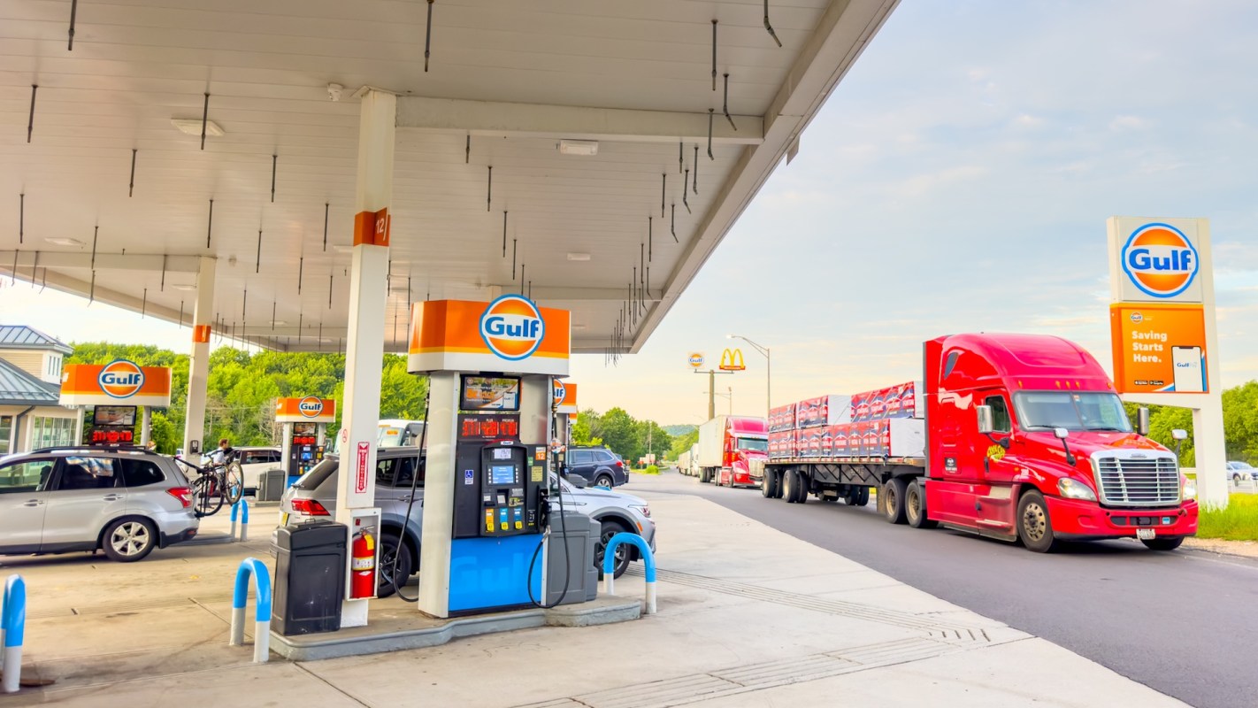 A gas station with vehicles, a bike rack, and a red truck on the road nearby.