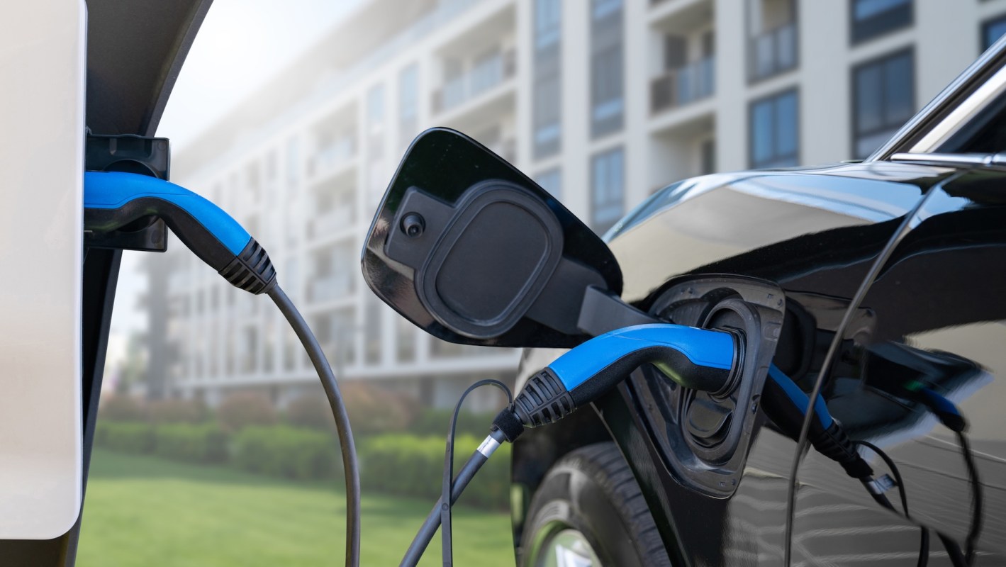 An electric vehicle is connected to a charging station in an urban area by an apartment building.