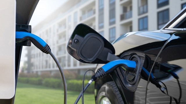 An electric vehicle is connected to a charging station in an urban area by an apartment building.