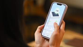 A person holds a smartphone displaying a solar panel monitoring app with various readings and statistics.