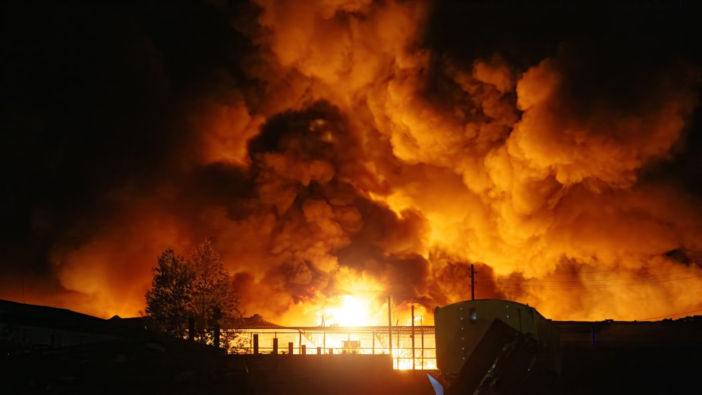A large fire emits bright flames and thick smoke against a dark sky.