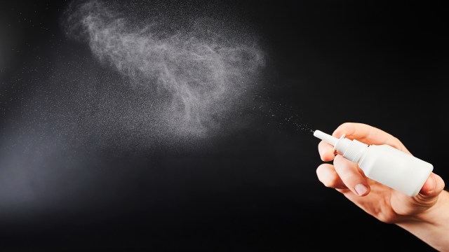 A hand holding a spray bottle releasing a fine mist against a dark background.