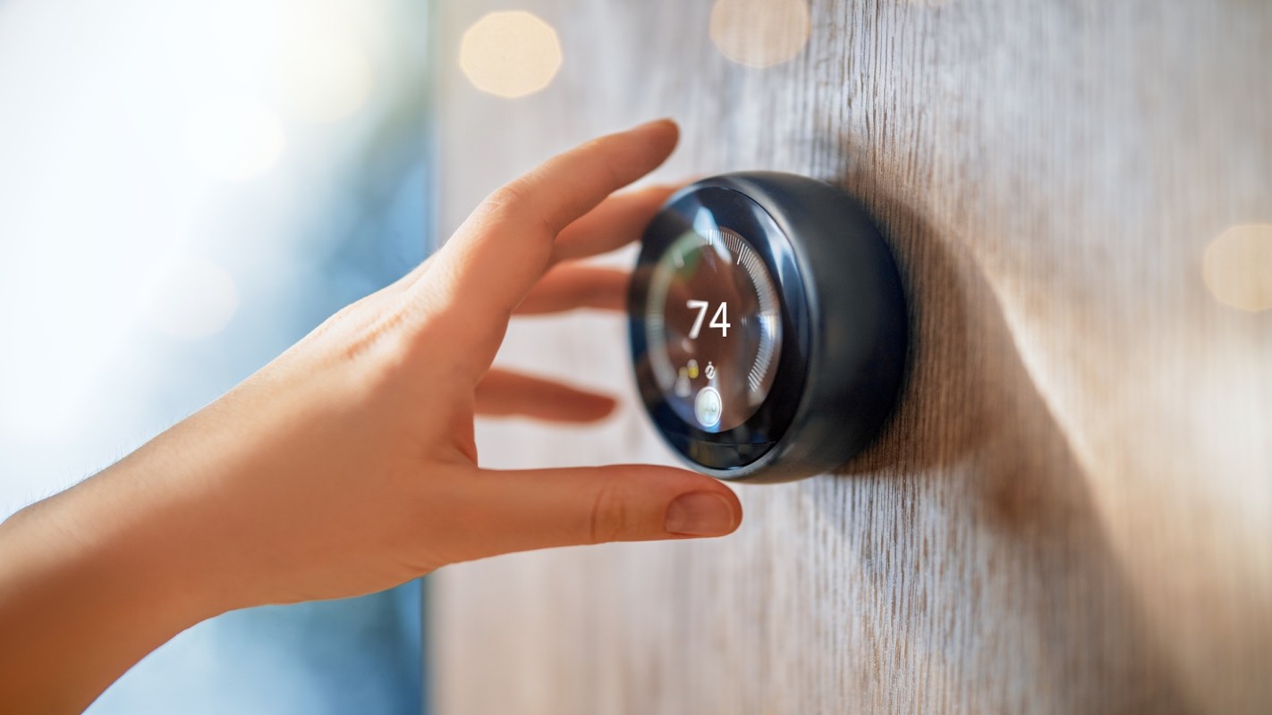 A hand adjusts a digital thermostat displaying the temperature setting.