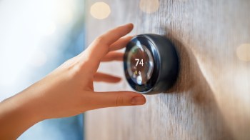 A hand adjusts a digital thermostat displaying the temperature setting.