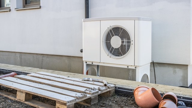 An outdoor air conditioning unit beside a wooden pallet and clay plant pots on the ground.