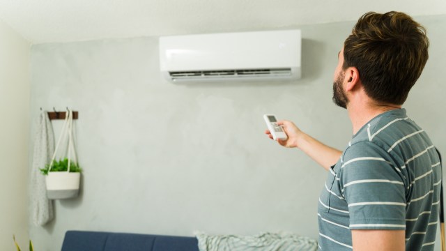 A man points a remote control at a wall-mounted mini split unit in a living room.