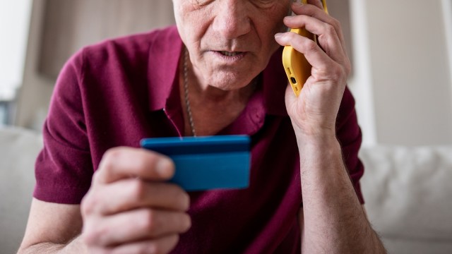 An older man holding a credit card and talking on the phone.