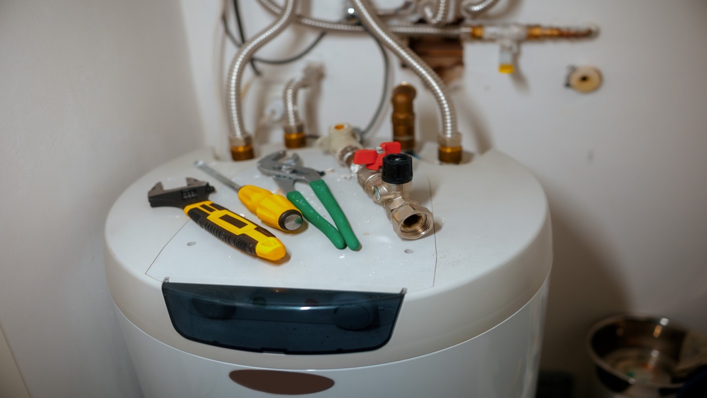 A water heater with tools and fittings placed on top.