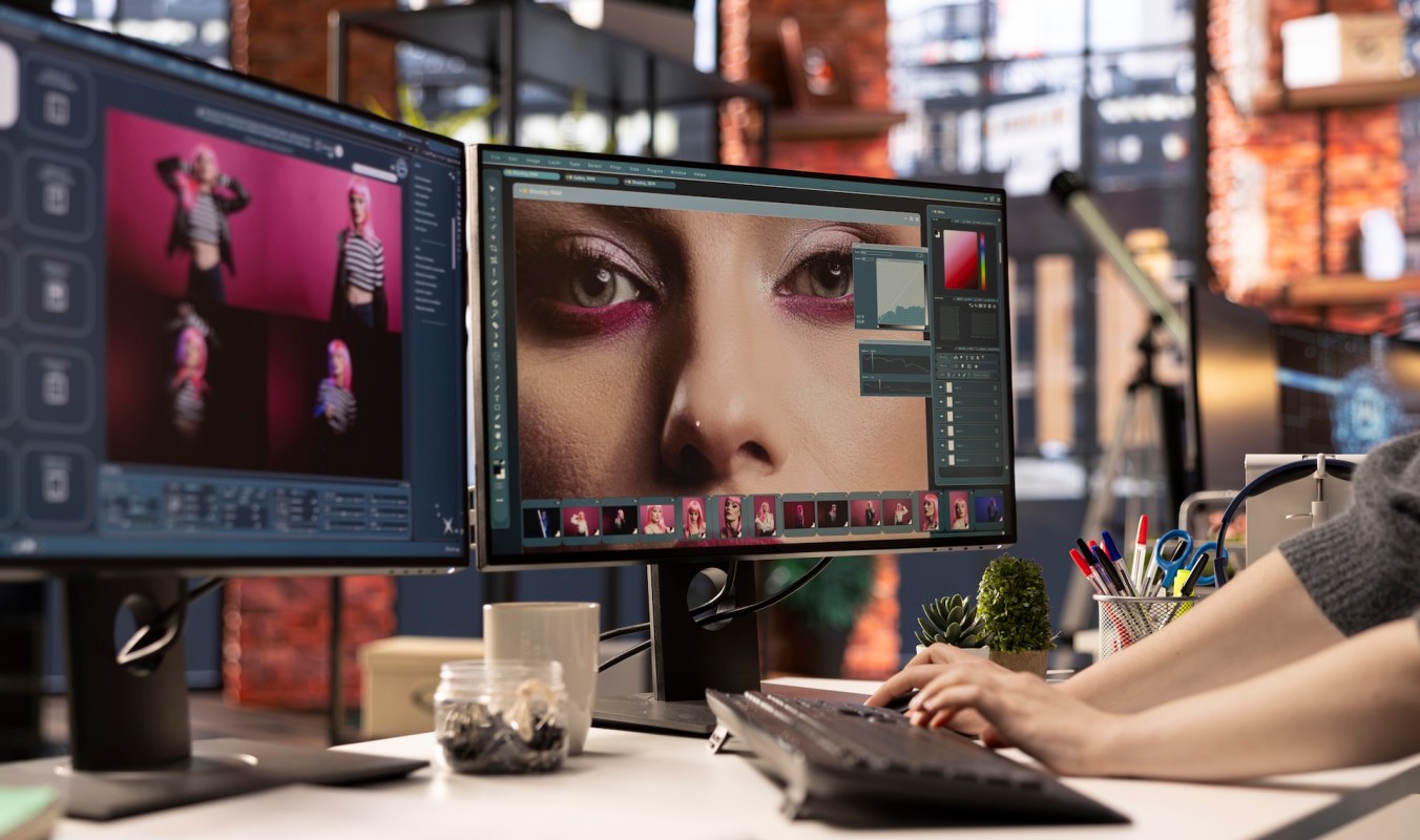 A person edits photos on dual monitors in a creative workspace.