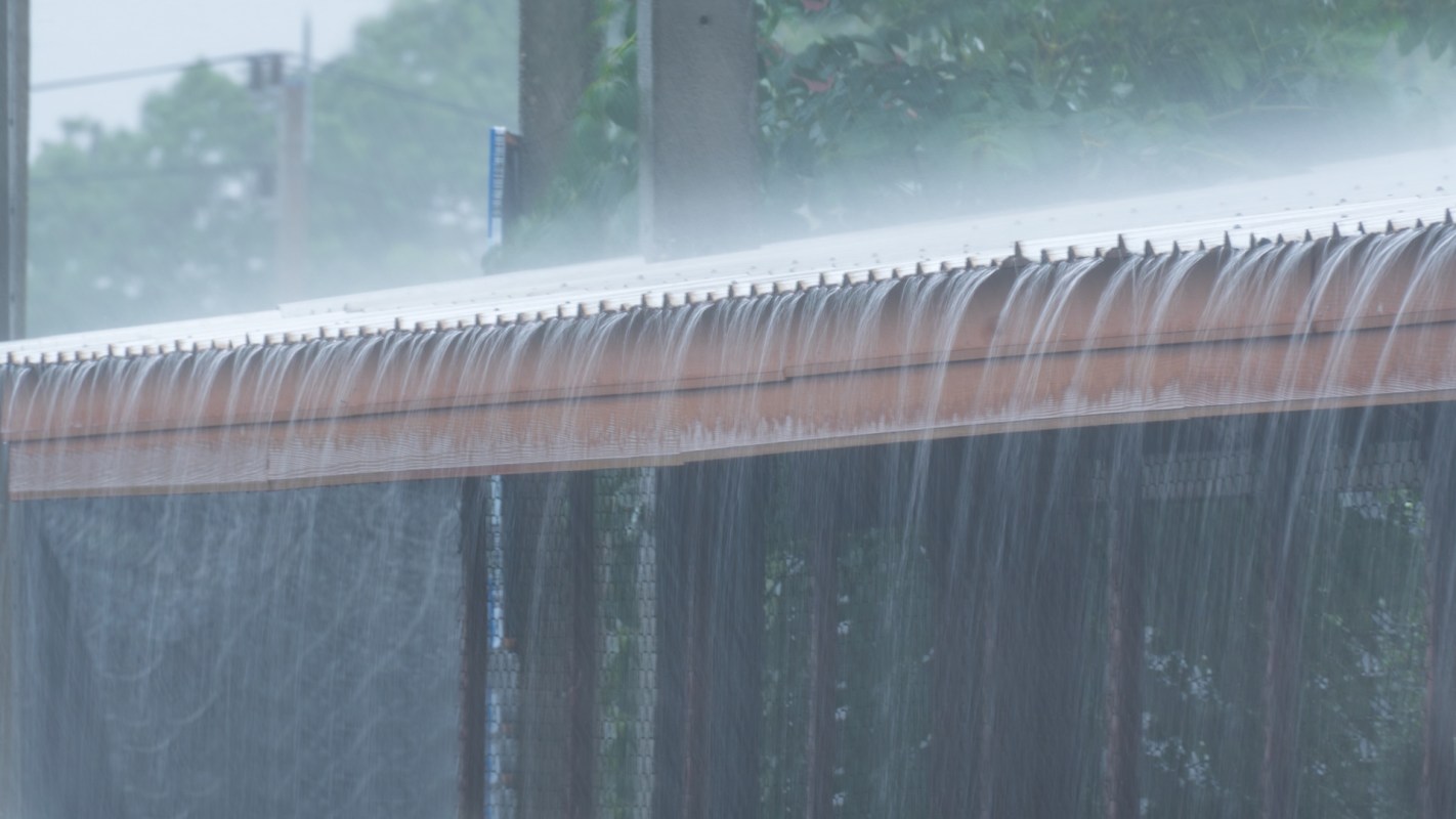Water flows over the edge of a roof during a heavy rain.