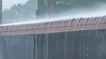Water flows over the edge of a roof during a heavy rain.
