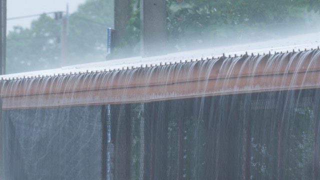 Water flows over the edge of a roof during a heavy rain.