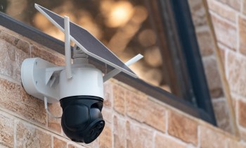A security camera with a solar panel mounted on a brick wall.