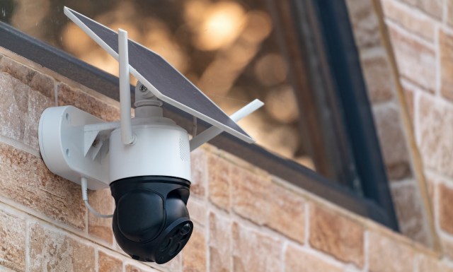 A security camera with a solar panel mounted on a brick wall.