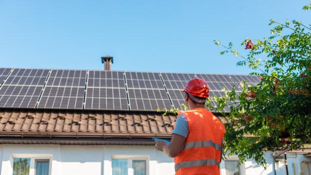 A worker inspecting solar panels on a rooftop.