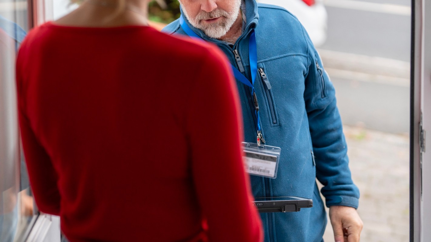 A man with a badge speaks to a person at a doorstep.