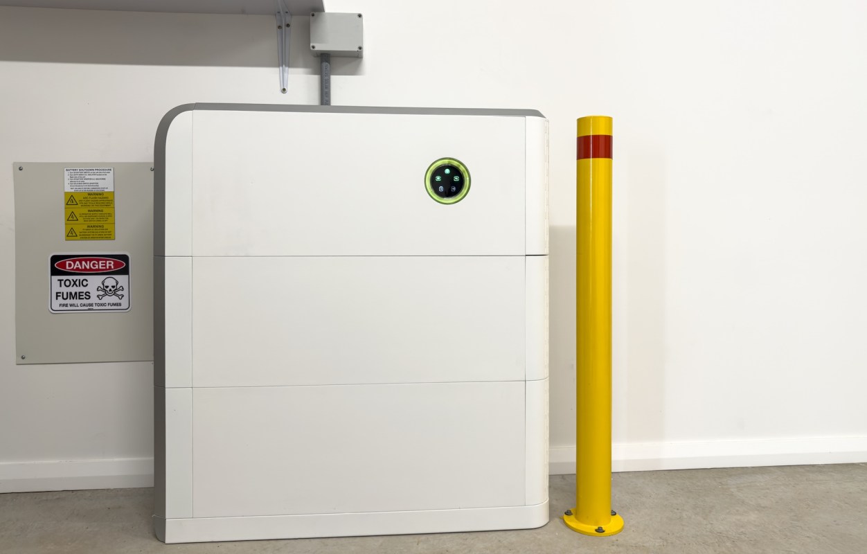 A large white storage unit next to a yellow safety bollard and warning signs on the wall.