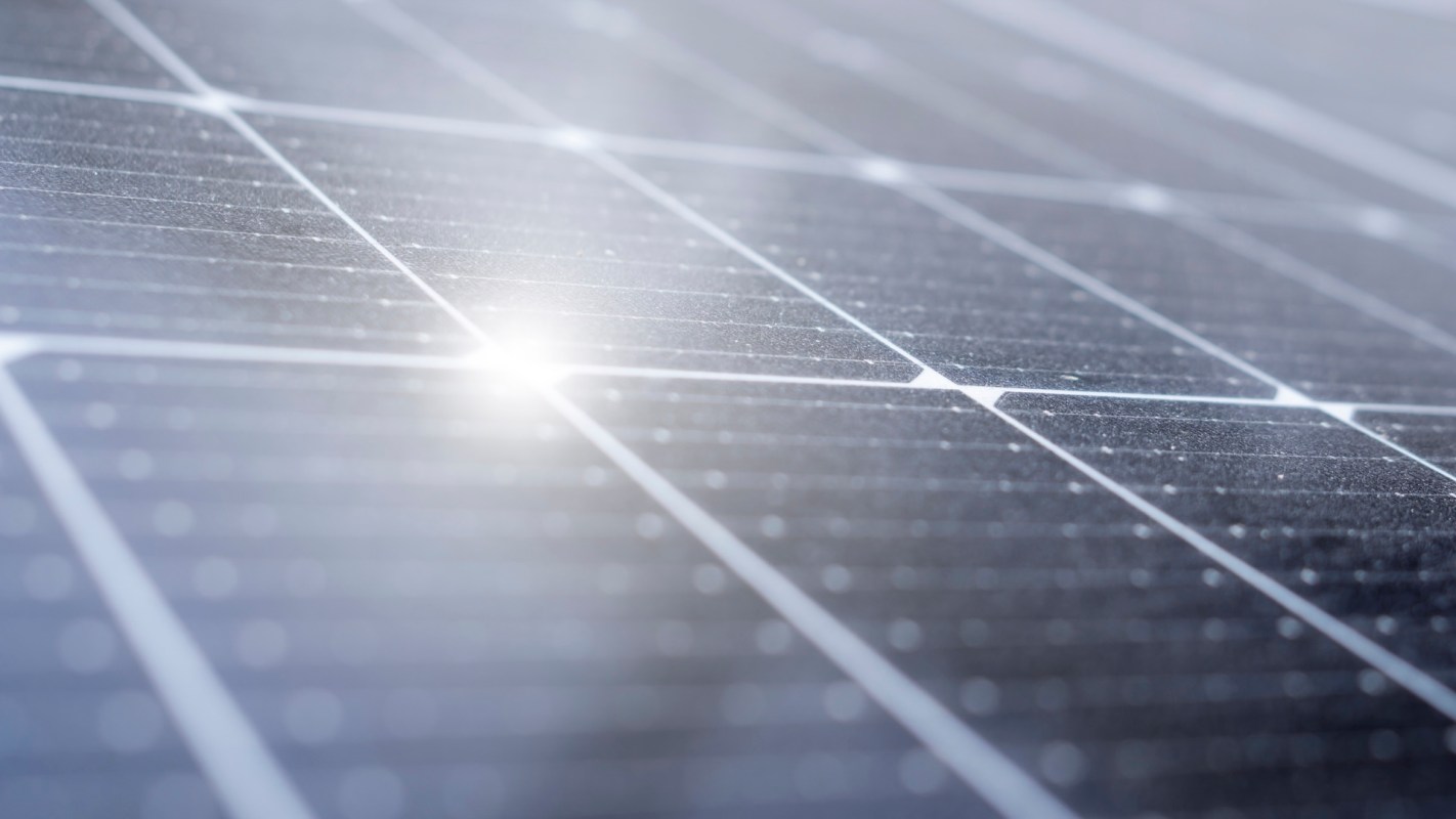A close-up of solar panel cells with reflective surfaces, with one bright point of sunlight in the middle.