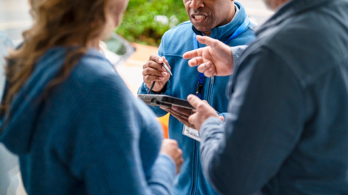 A salesman at the door discussing something with a tablet and a pen in hand to two people.