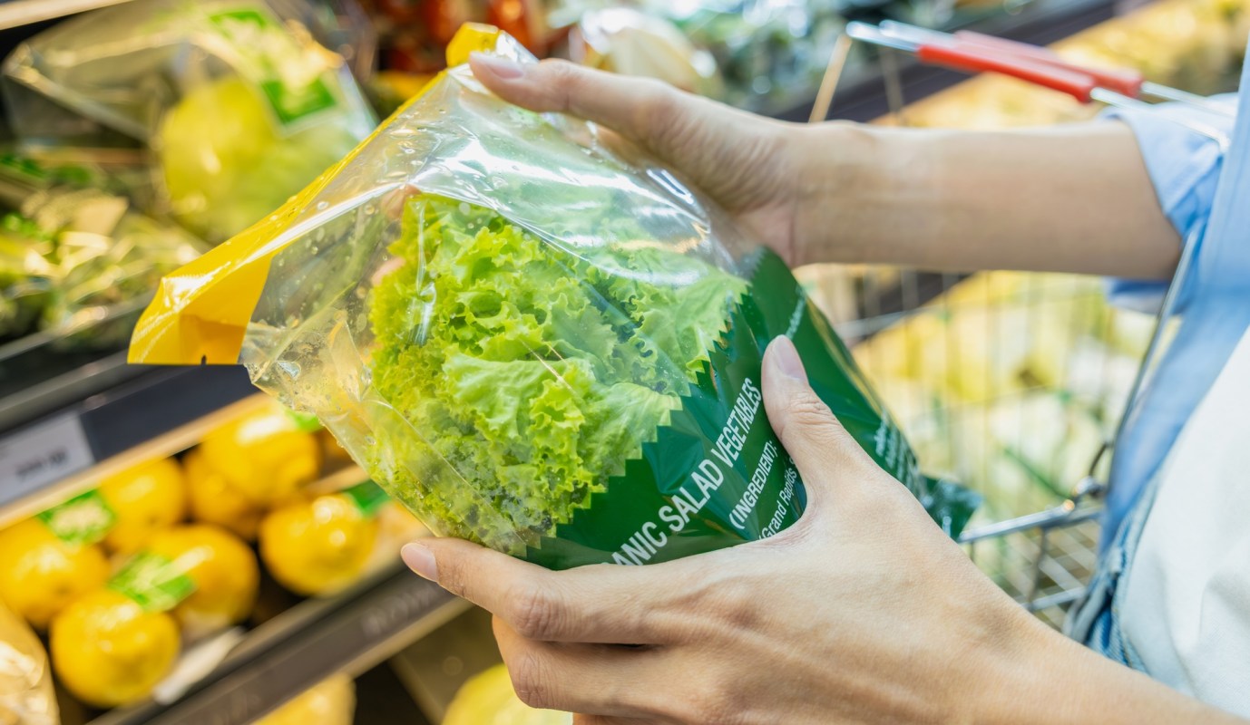 A person holds a bag of organic salad greens in a grocery store.