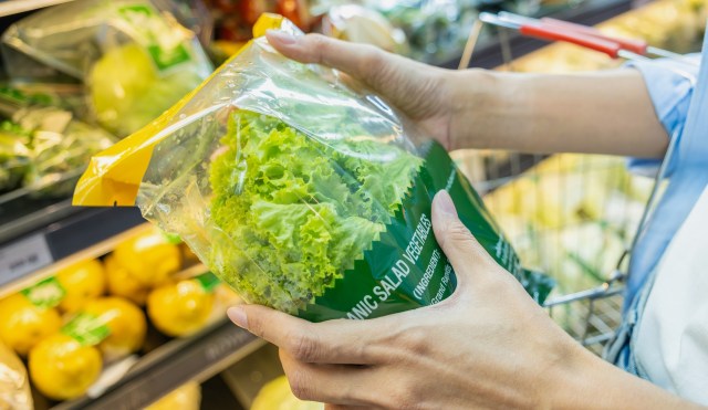 A person holds a bag of organic salad greens in a grocery store.