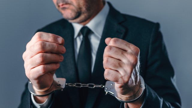 A person in a suit holds their hands in handcuffs.