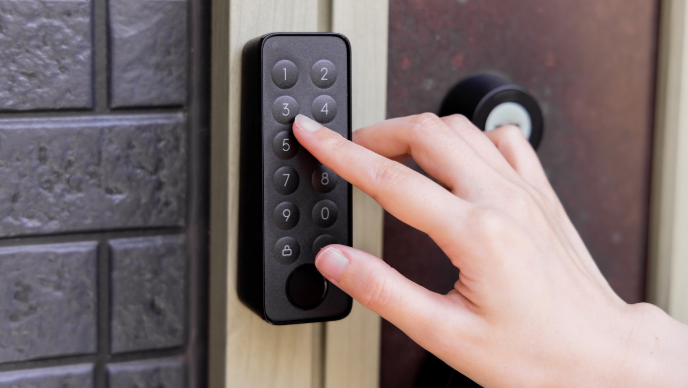 A hand is pressing numbers on a digital keypad next to a door lock.