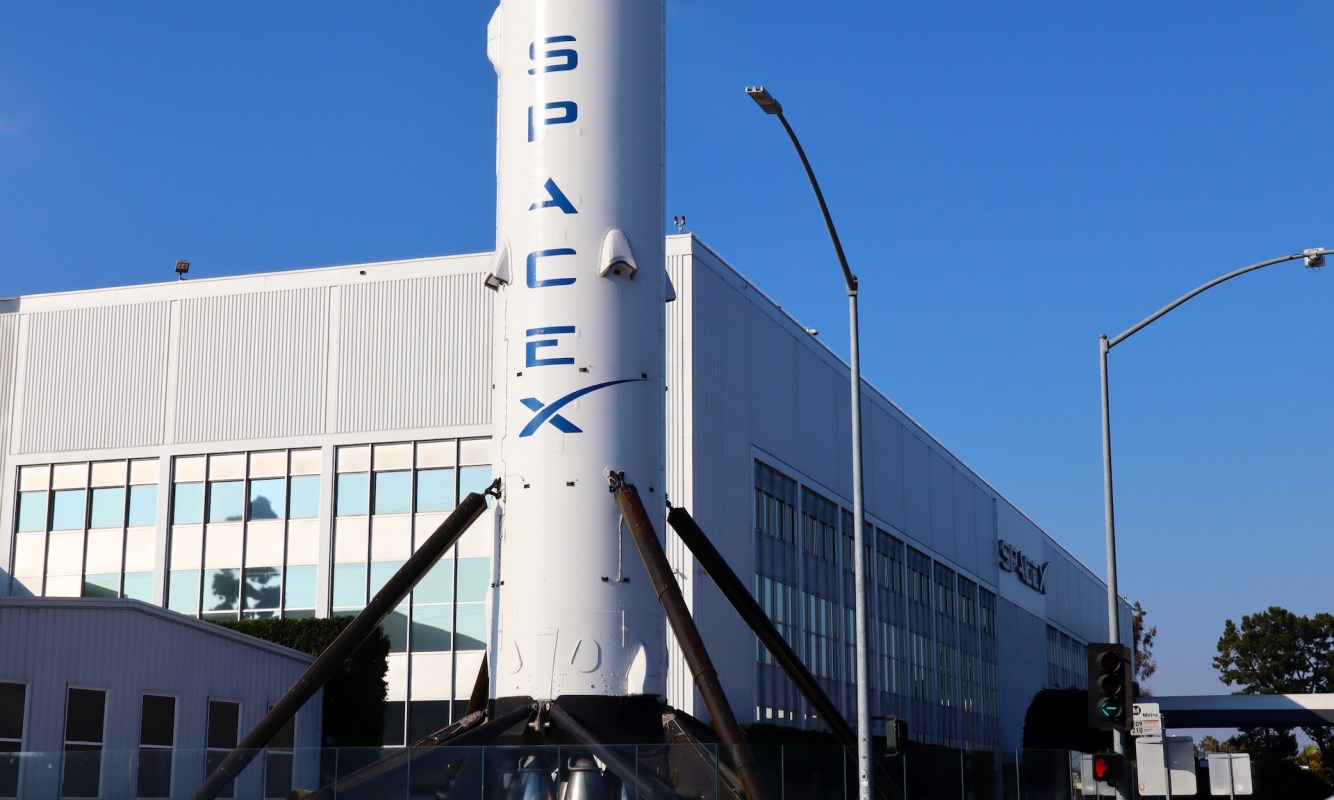 A SpaceX rocket is displayed outside a building with large windows.