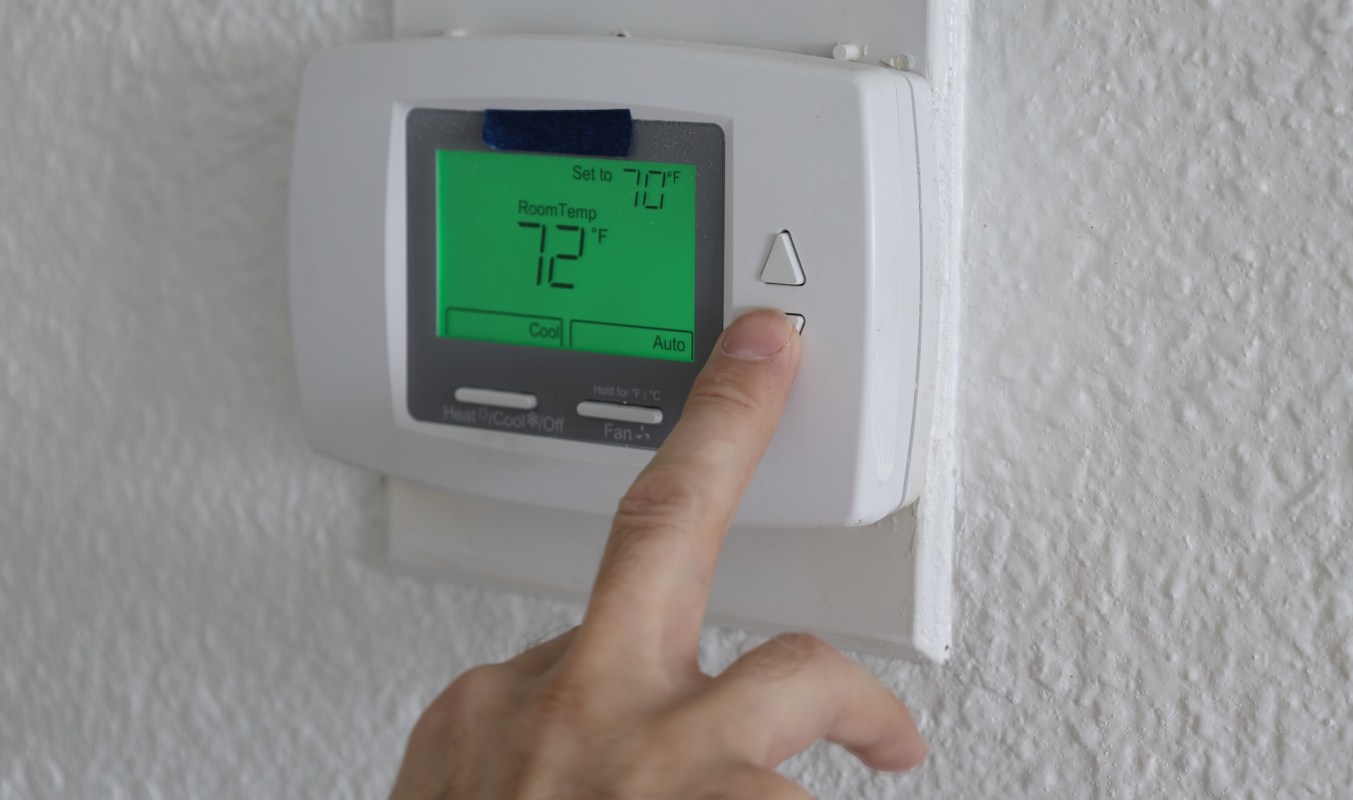 A person adjusting a digital thermostat displaying the current and set room temperatures.