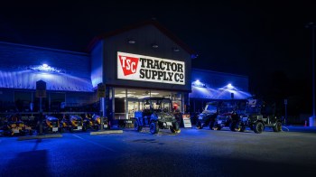 A Tractor Supply Co. store with various vehicles displayed outside, illuminated by blue lighting at night.