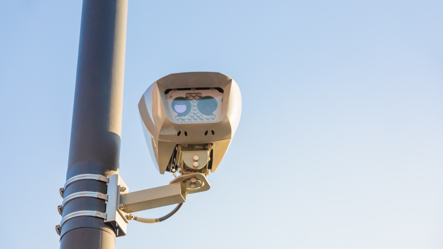 A surveillance camera mounted on a pole against a clear blue sky.