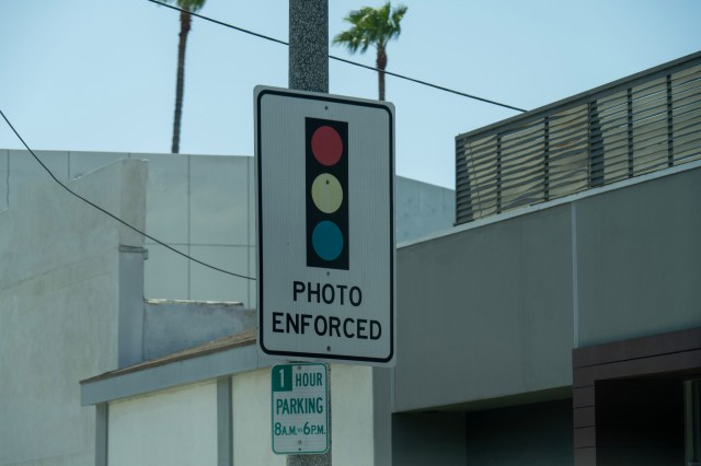 A traffic sign indicating "Photo Enforced" with red, yellow, and blue lights.