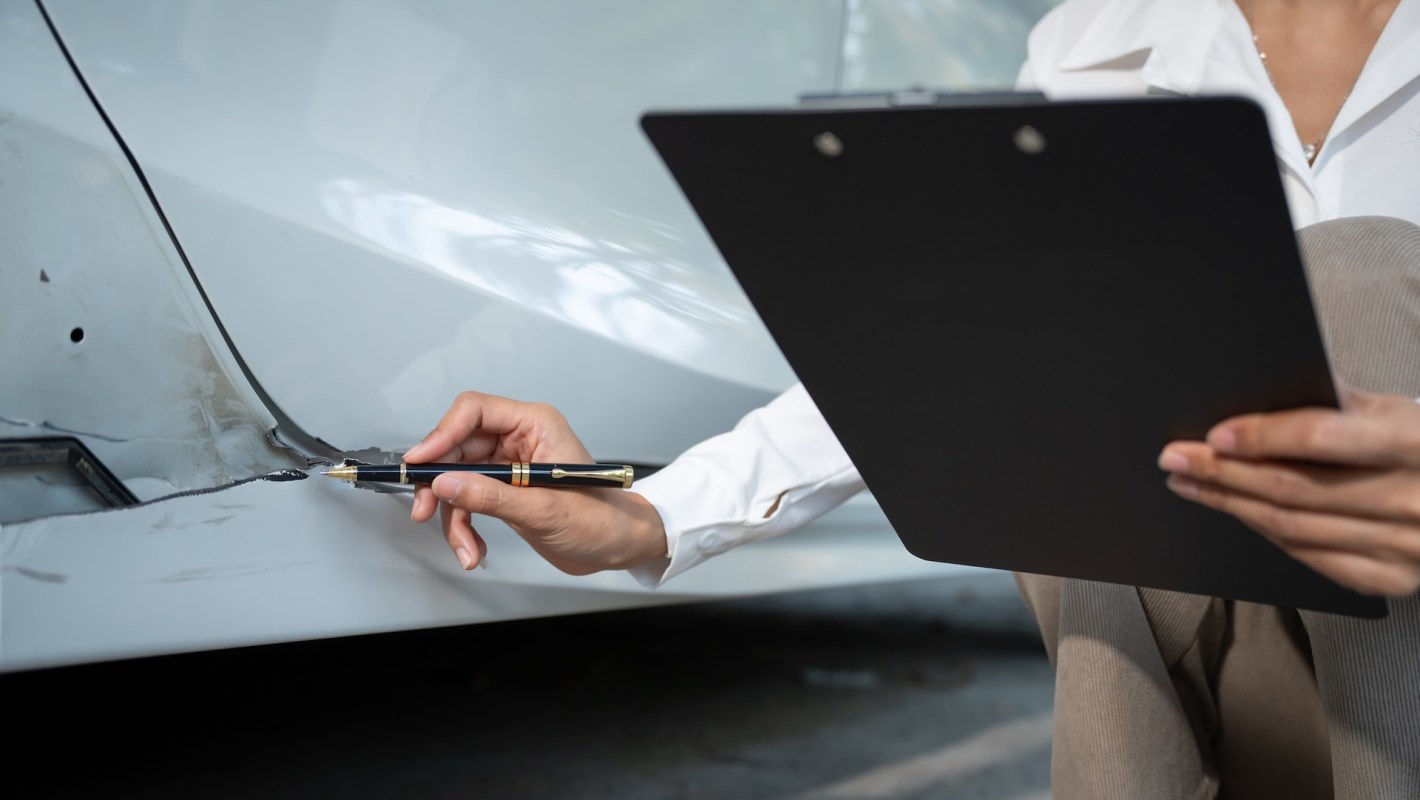 A person inspects and takes notes on a damaged area of a vehicle.