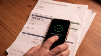 A smartphone displaying a payment confirmation is next to an electricity bill on a wooden surface.