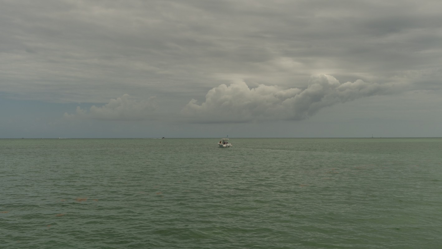 A boat travels across a calm, green sea under a cloudy sky.