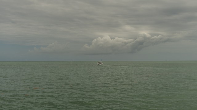 A boat travels across a calm, green sea under a cloudy sky.