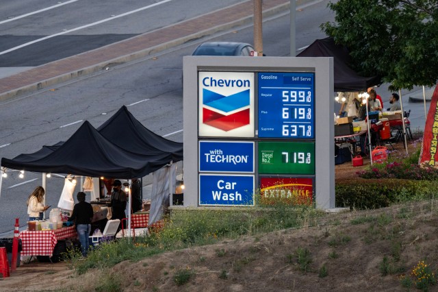 A Chevron gas station sign displays fuel prices alongside food vendor tents.