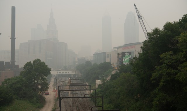 A cityscape shrouded in haze, featuring skyscrapers and railway tracks in the foreground.