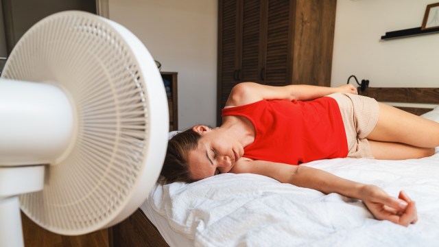 A woman on a bed using a fan to cool down.