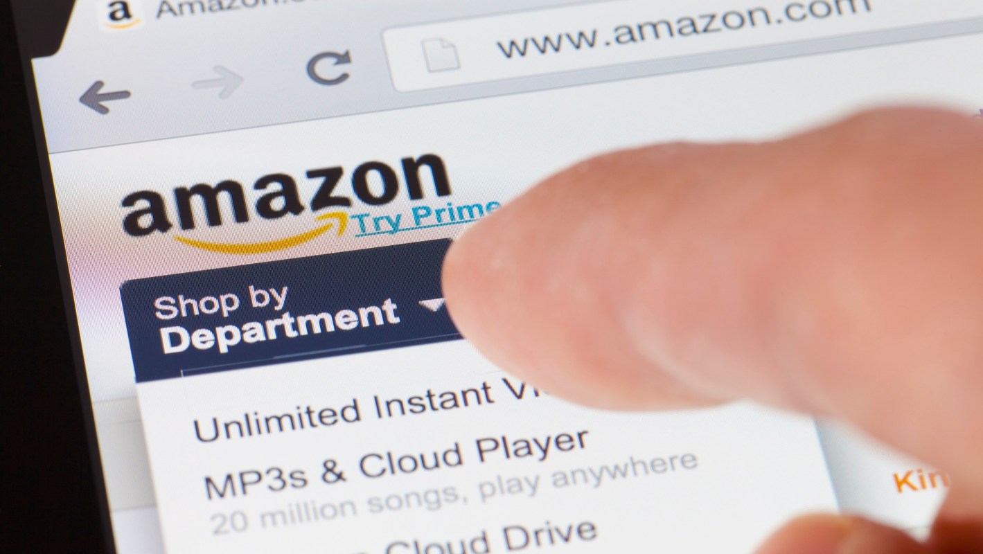 A hand tapping on a smartphone screen displaying the Amazon shopping website.