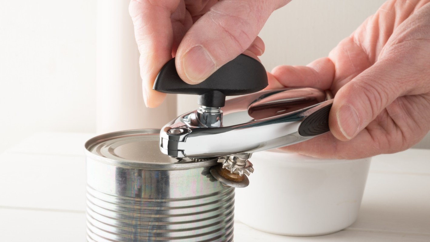 A hand using a can opener on a metal can.