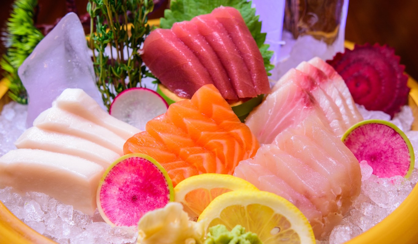 A variety of sashimi and garnishes arranged on ice with lemon and colorful radishes.