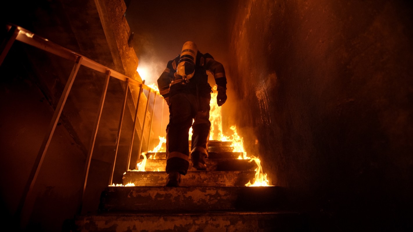 A firefighter ascends a staircase engulfed in flames.